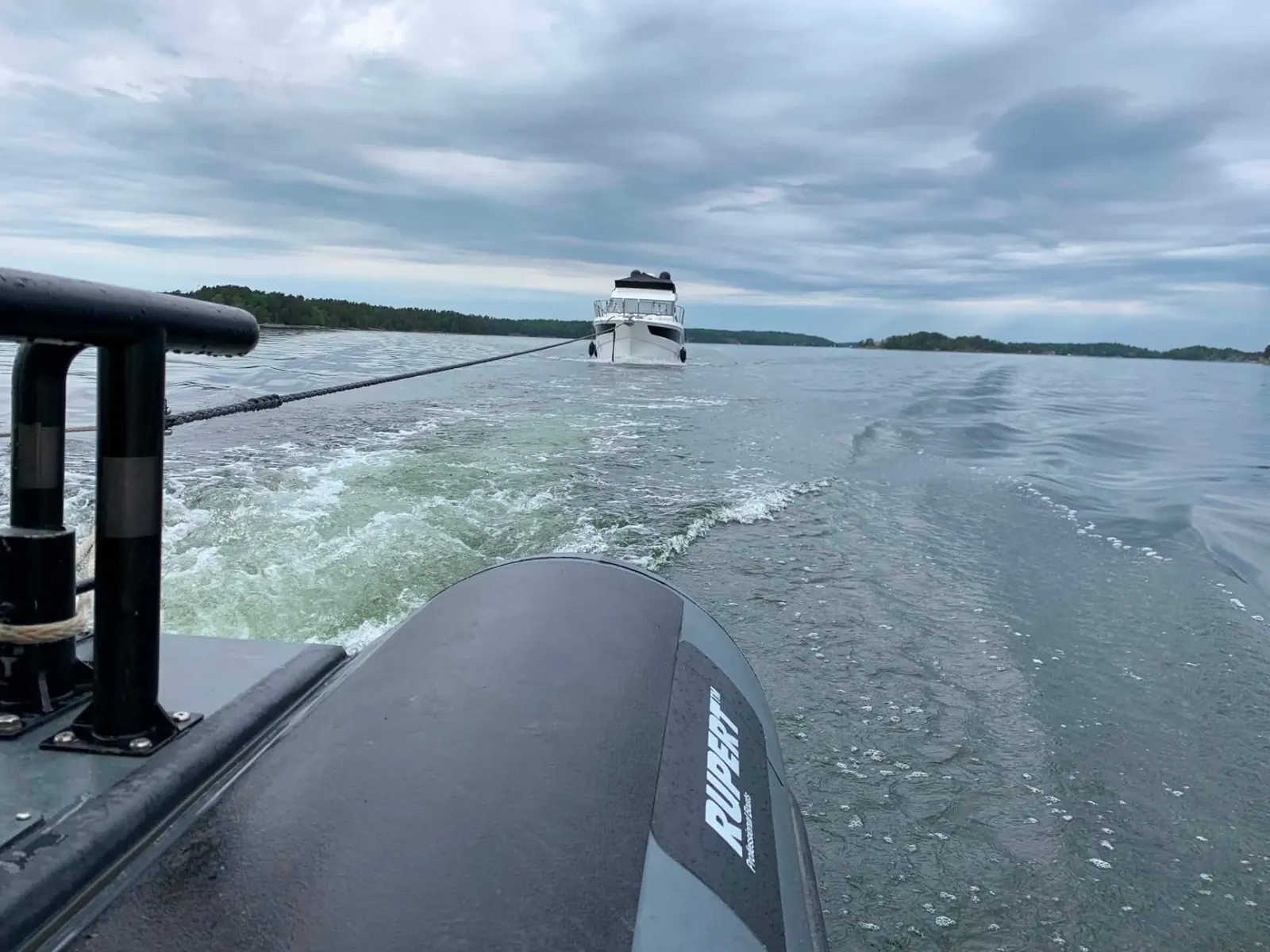 Motorbåt bogseras bakom arbetsbåt i Stockholms skärgård